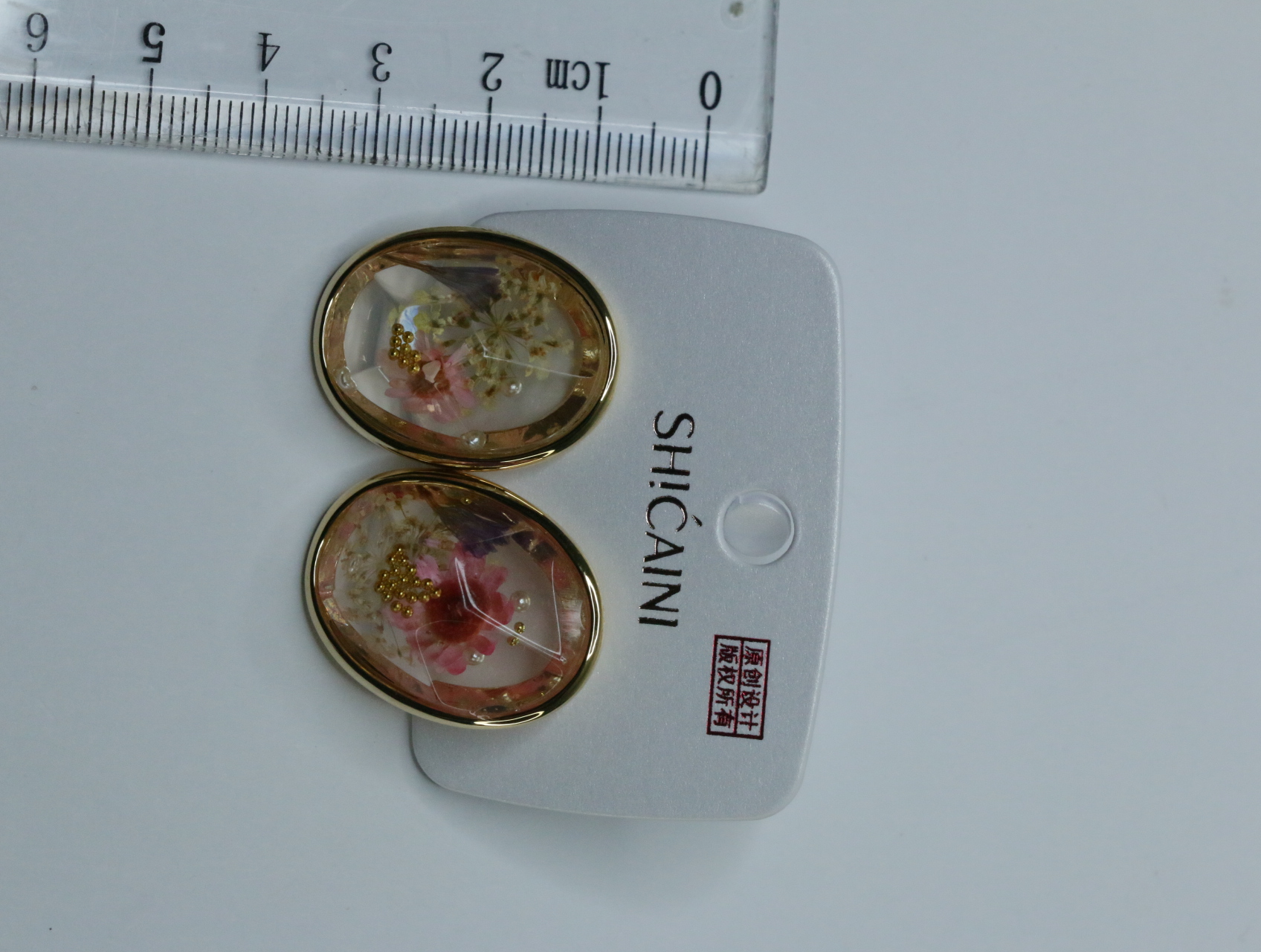 Pendientes ovalados florales junto a una regla — lote de bisutería originales, detalle del acabado · Lotes Bisutería (118)