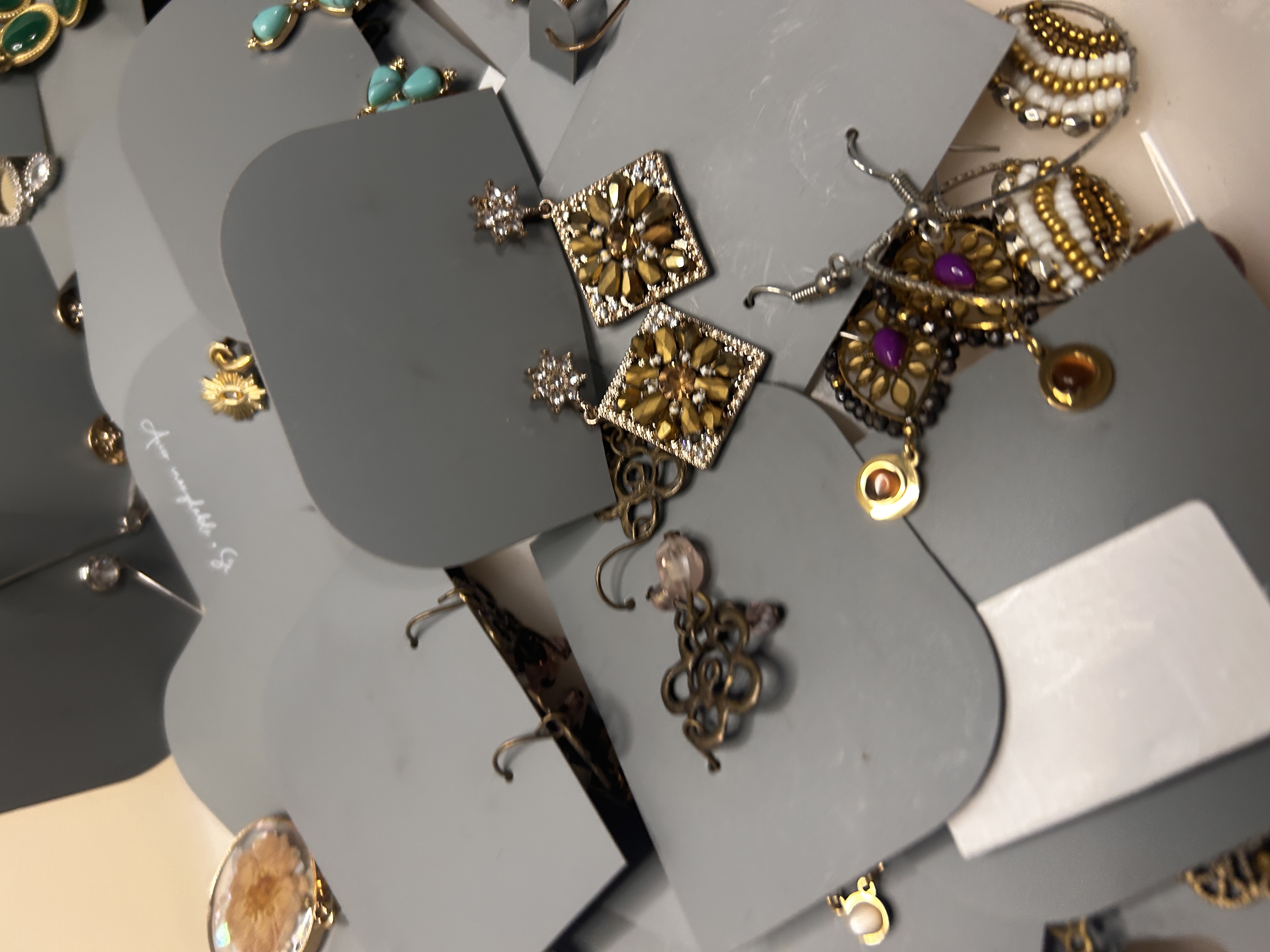 Primer plano de pendientes colgantes variados en tarjetas grises, incluyendo diseños elaborados de tono dorado y con joyas, en una bandeja blanca.