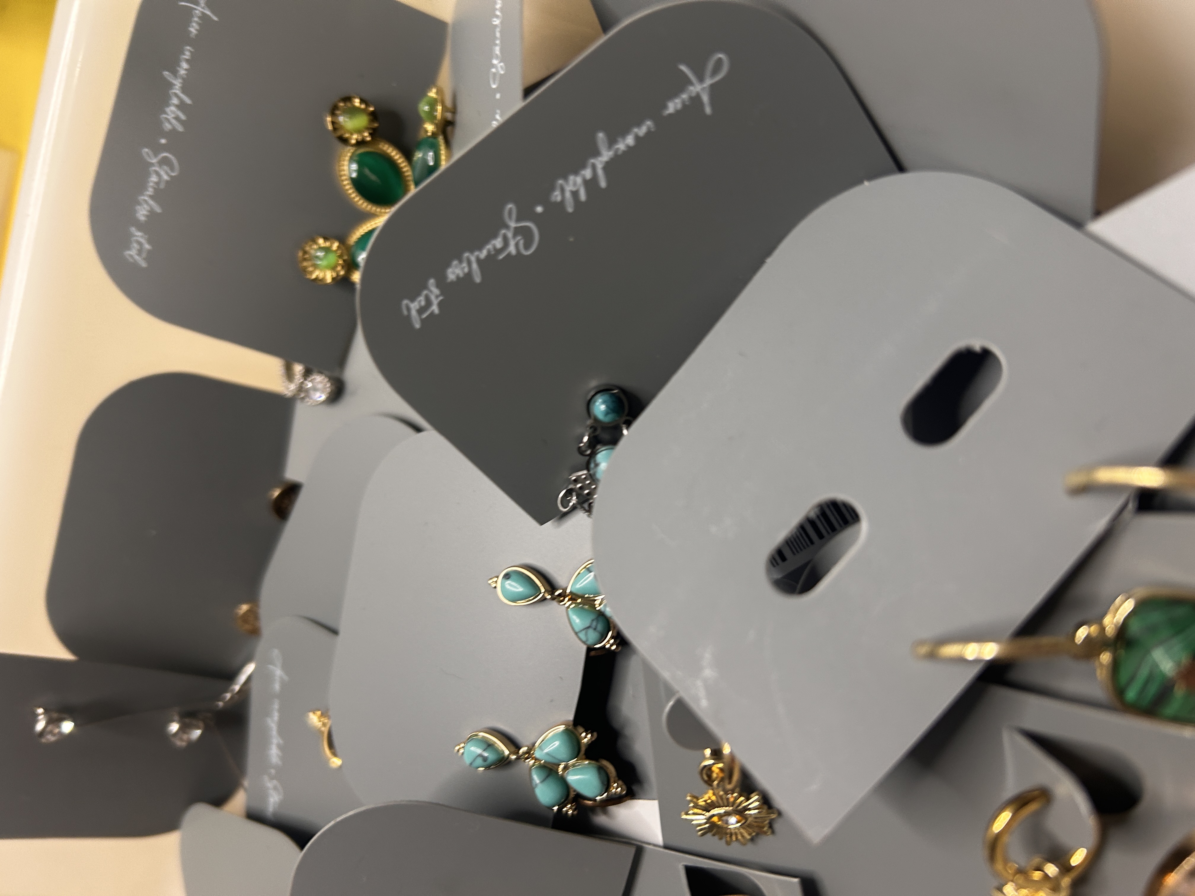 Otro primer plano del lote de pendientes, mostrando varios diseños de acero inoxidable que incluyen pendientes de grupos de turquesas y de imitación de malaquita verde en tarjetas grises.