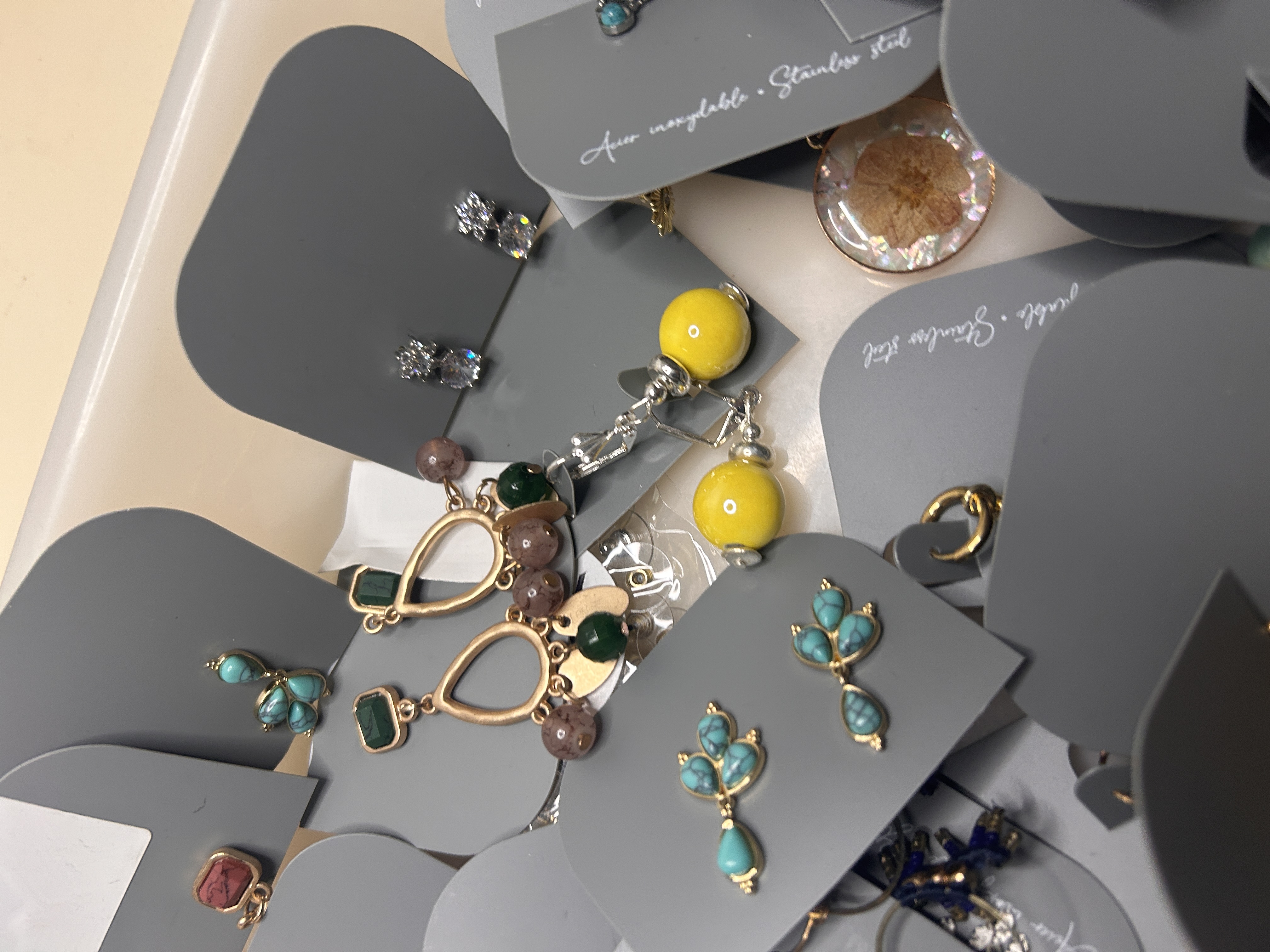 Pendientes de bisutería surtidos en una bandeja, mostrando diseños como pendientes dorados con múltiples cuentas pequeñas, pendientes esféricos de color amarillo brillante y delicados pendientes de turquesa.