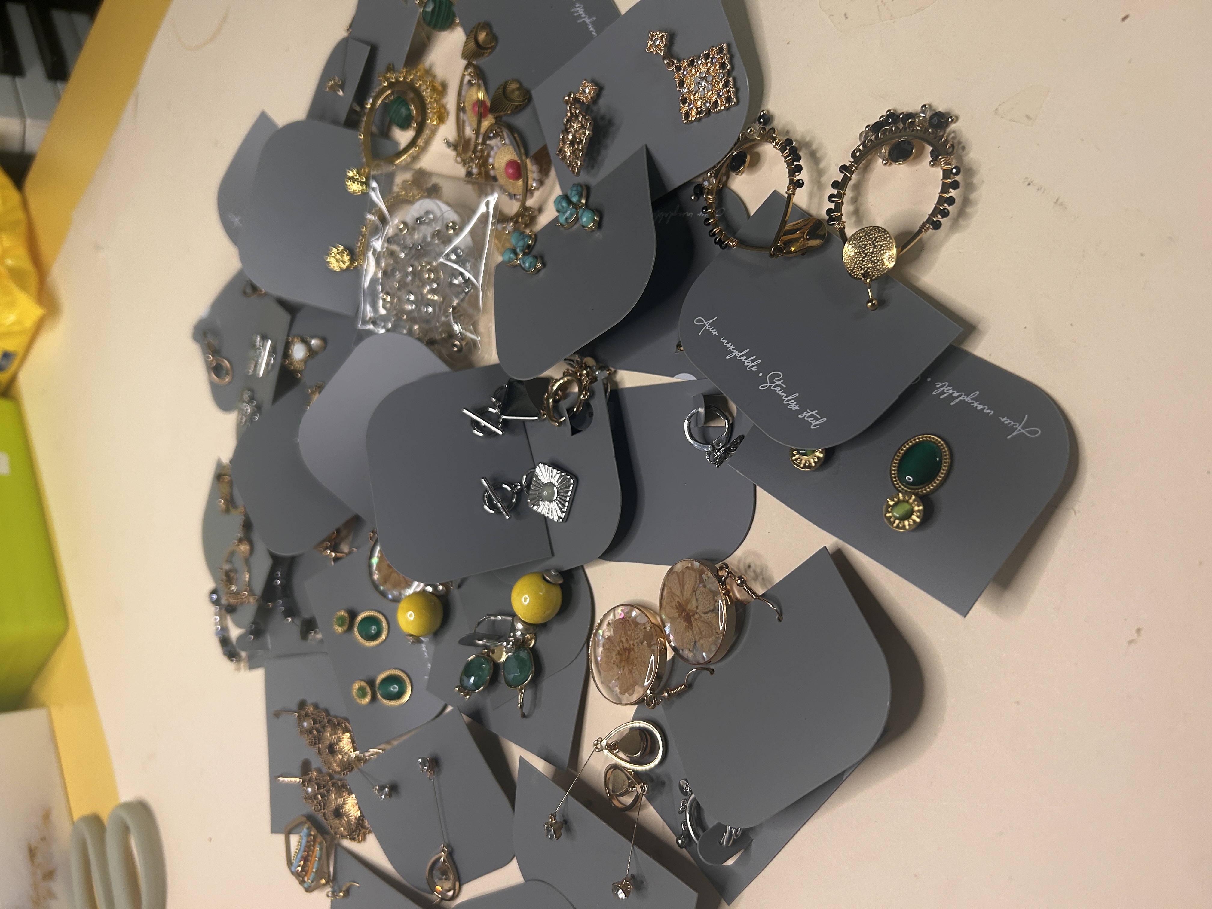 Vista ligeramente en ángulo del lote de bisutería diversa, destacando diferentes estilos de pendientes como aros, botones con piedras de colores y diseños colgantes, todos en tarjetas grises.