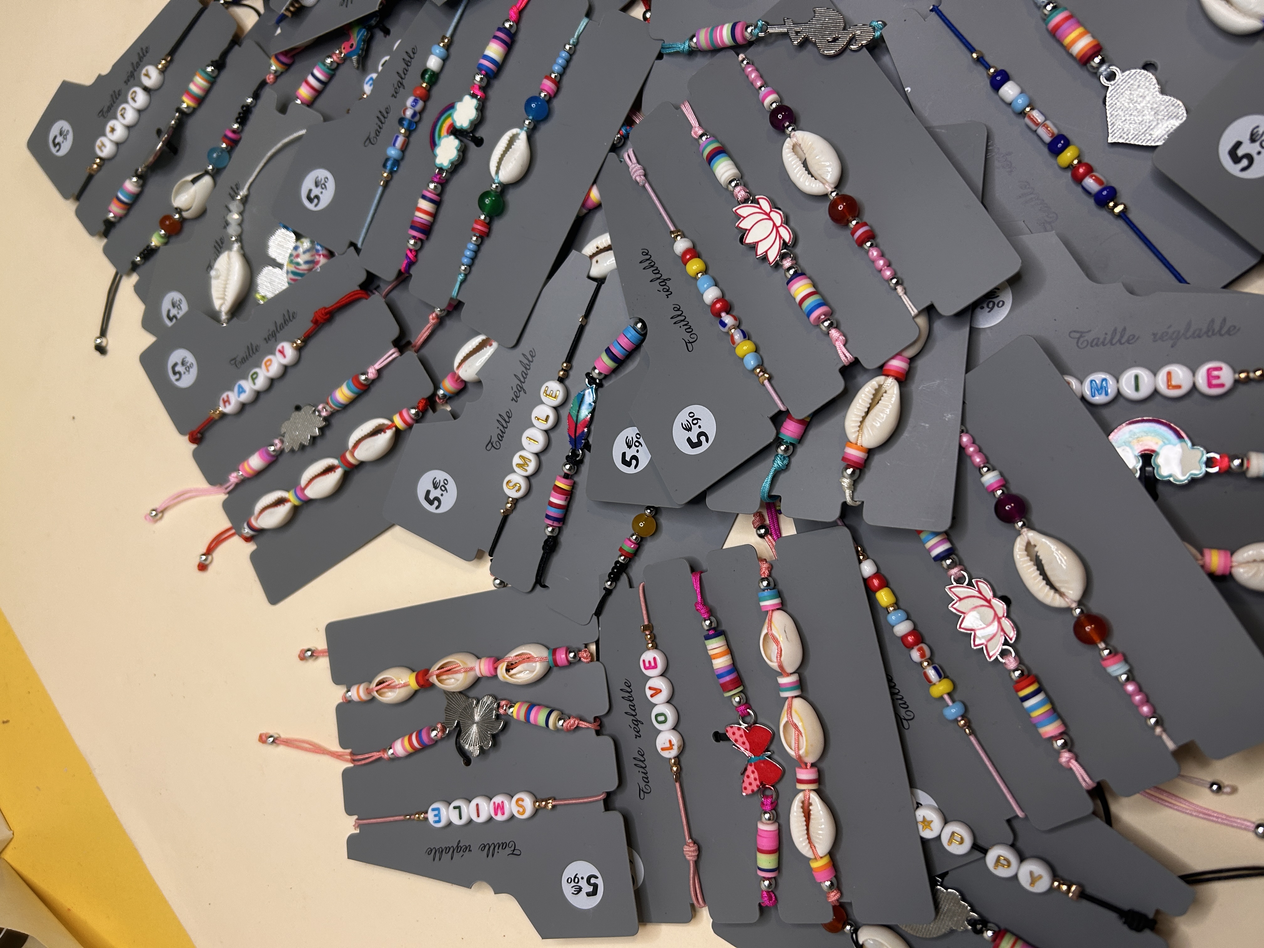 Otra vista de cerca del lote de pulseras, mostrando variedad en diseños, incluyendo charms de loto, diferentes combinaciones de colores y abalorios con las palabras 'LOVE' y 'SMILE'.