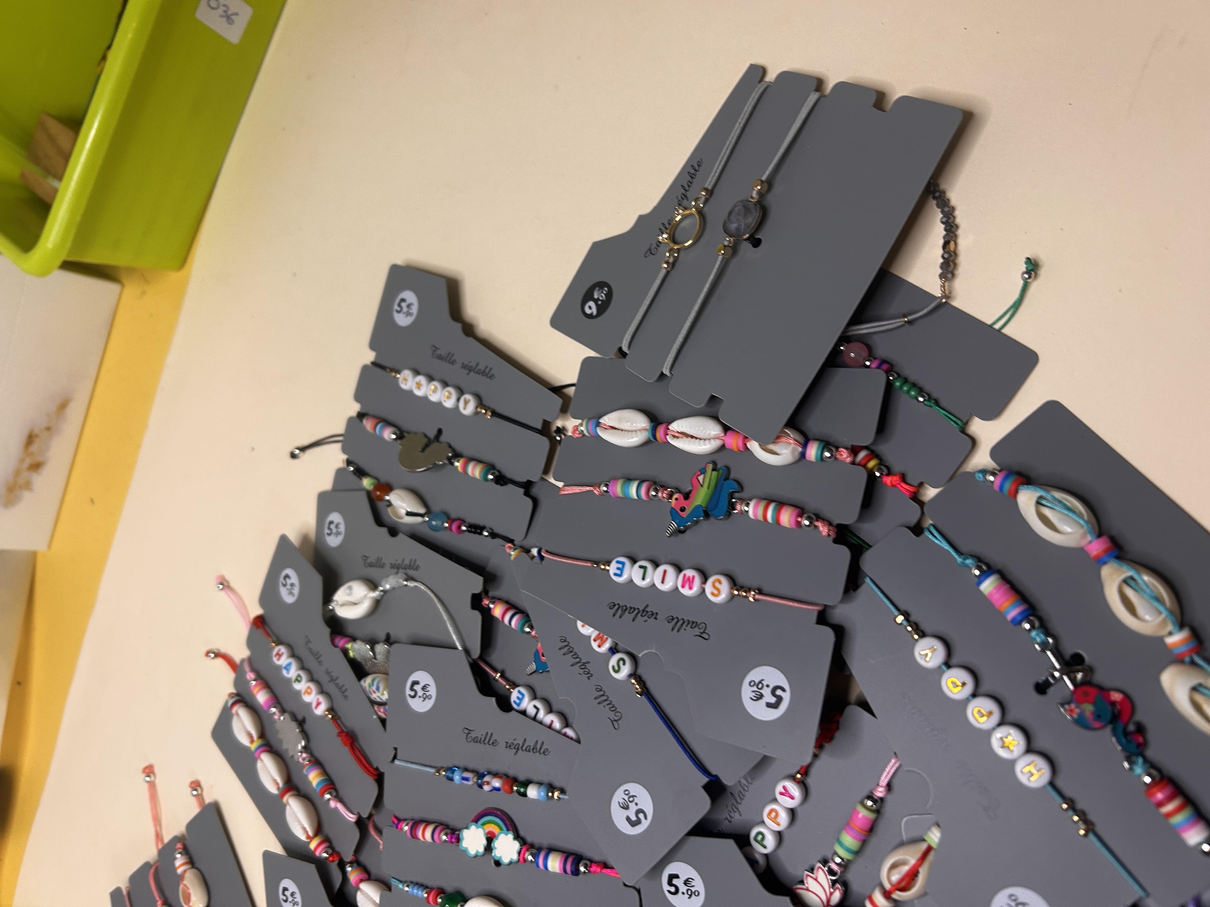 Vista angular del lote de pulseras, mostrando algunas con charms de arcoíris y abalorios de emojis, junto con los diseños de conchas cowrie y sugiriendo detalles del embalaje.