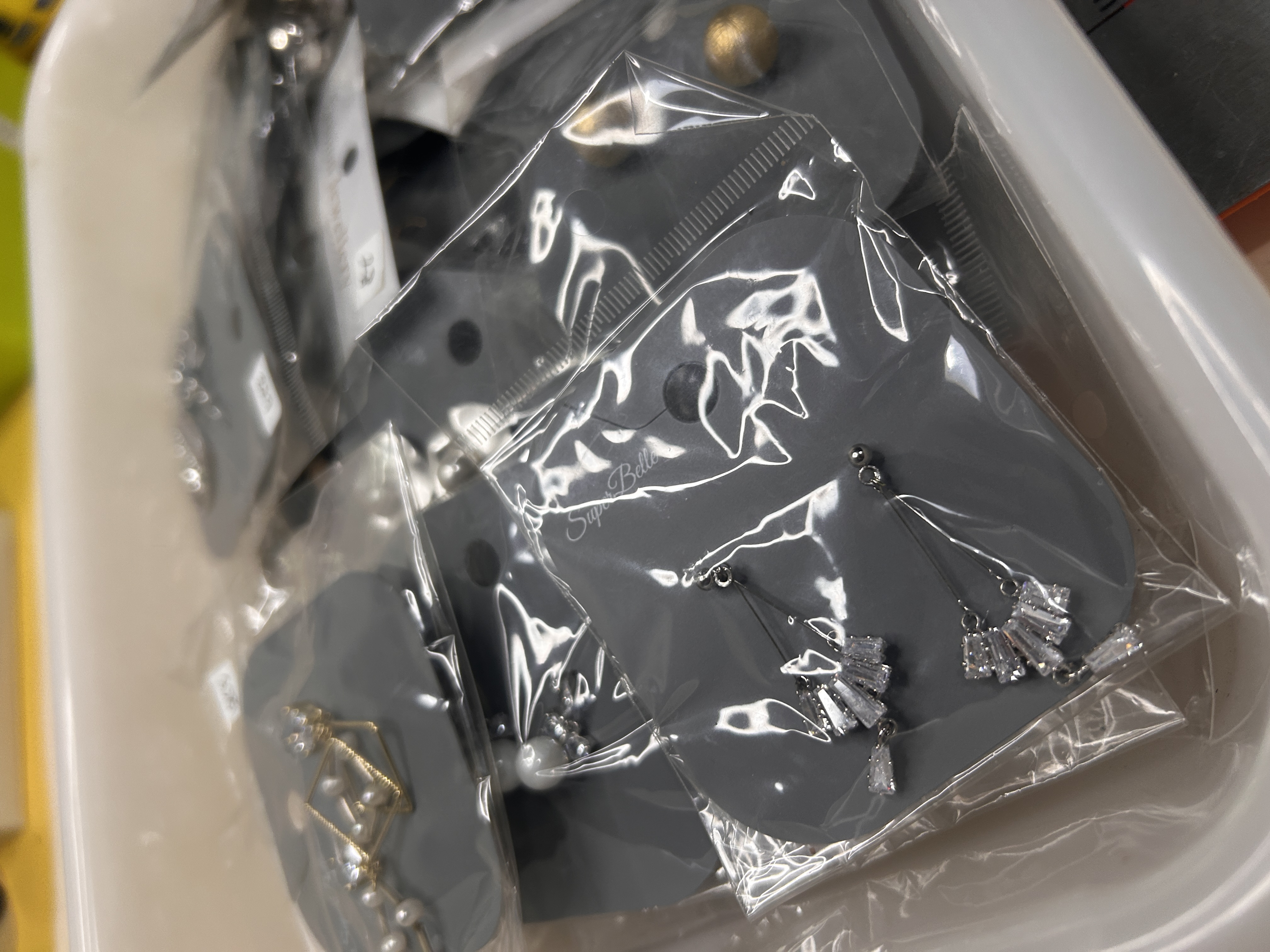Primer plano de varios pendientes de bisutería empaquetados individualmente en una bandeja, mostrando pendientes colgantes plateados con cristales transparentes
