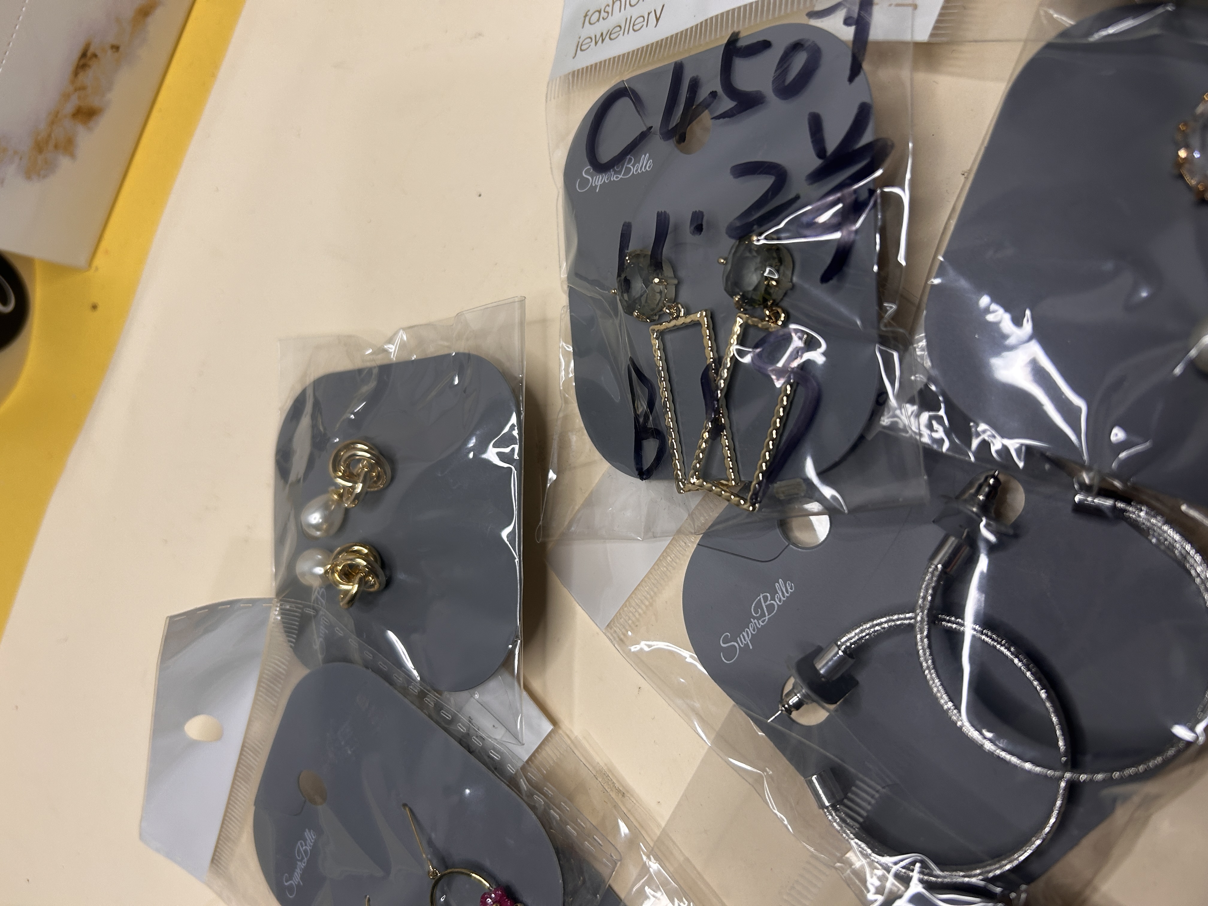 Selección de pendientes de bisutería con aros plateados, studs dorados anudados y diseños geométricos rectangulares, cada uno embolsado.