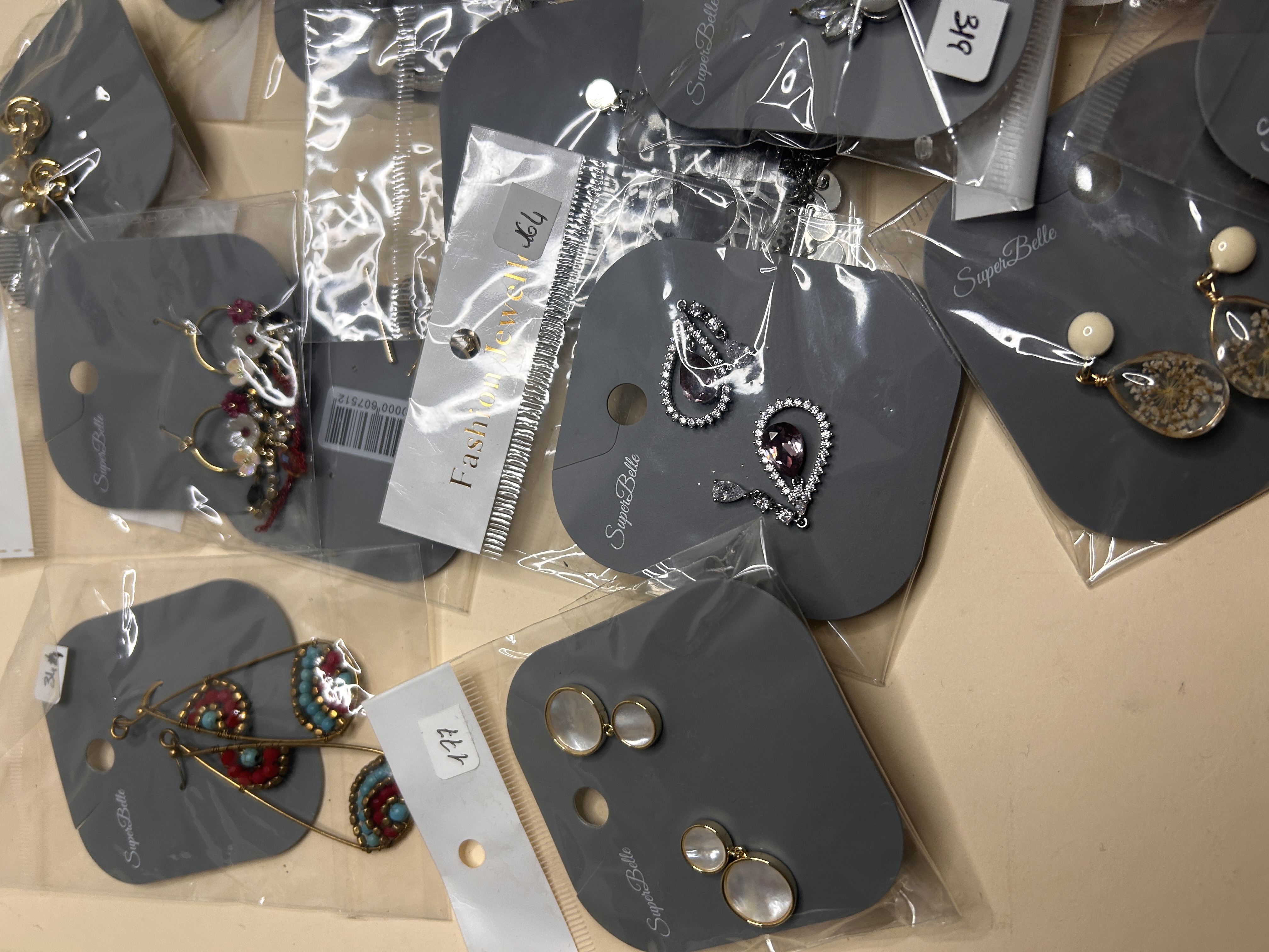 Variedad de pendientes de bisutería en tarjetas grises, mostrando diseños como intrincadas gotas plateadas con piedras y formas de lágrima más grandes con patrones naturales.