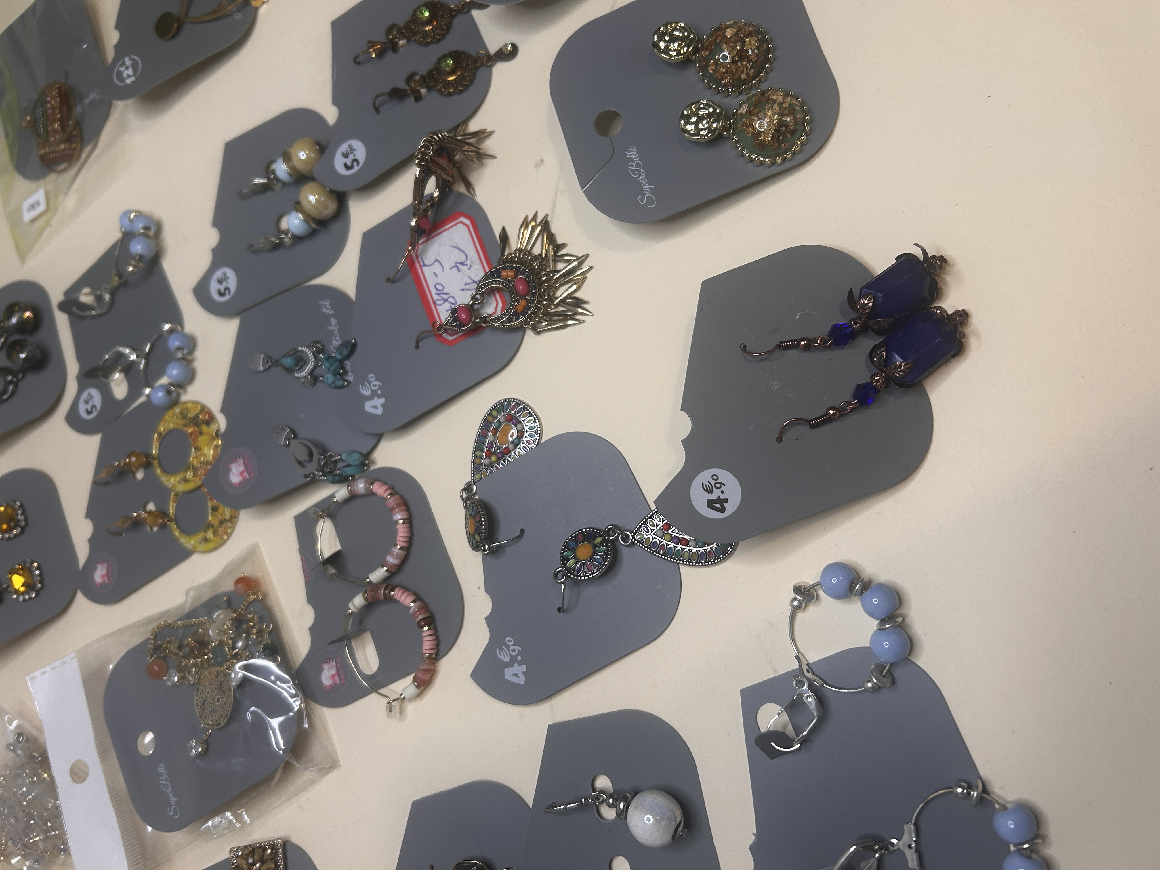 Otra toma de cerca de pendientes de bisutería, mostrando una variedad de estilos como colgantes ornamentados, aros grandes y coloridos, y diseños pequeños con cuentas, algunos con etiquetas de precio.