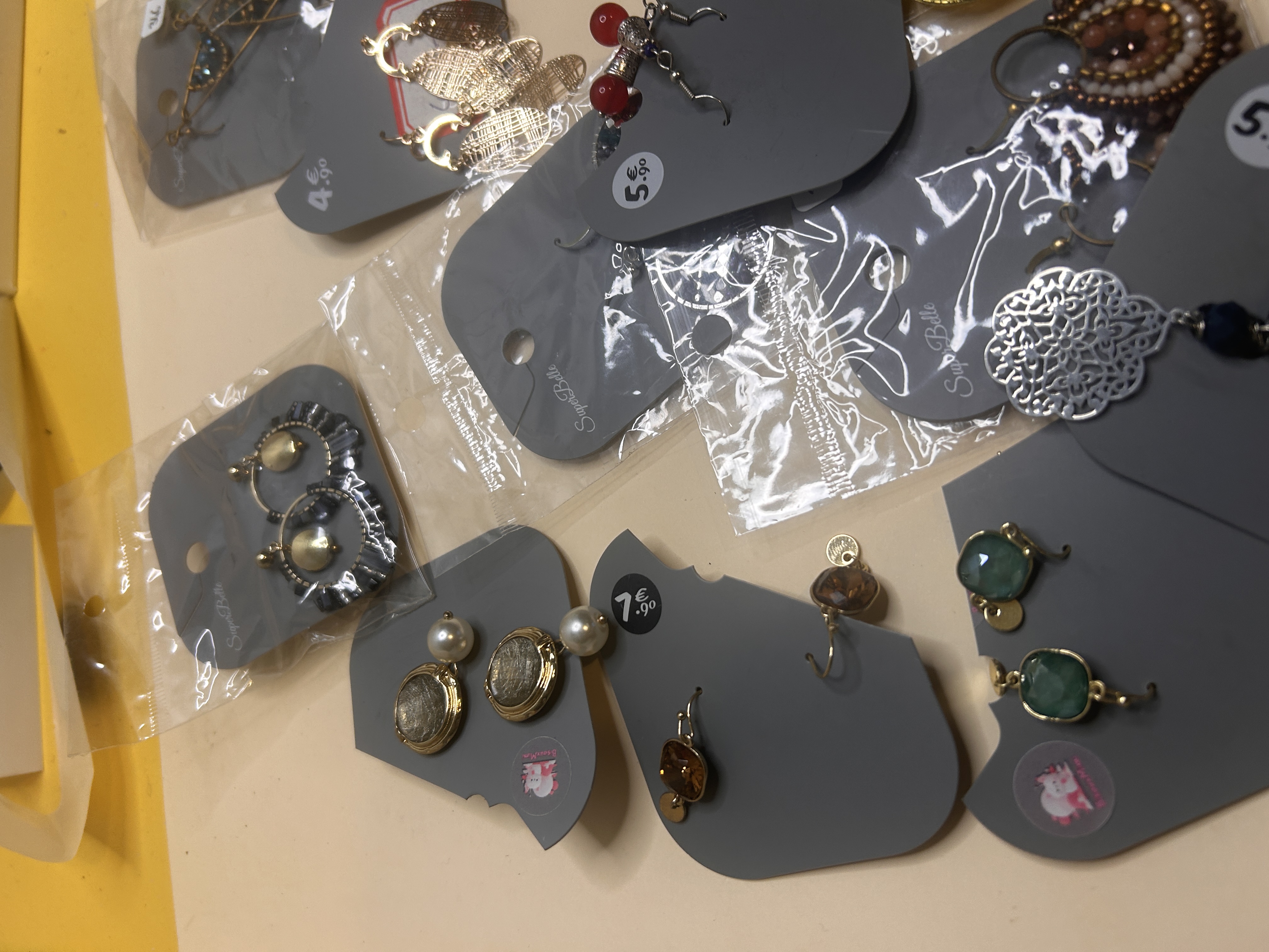Toma de primer plano que revela más diseños de pendientes, incluyendo botones de perla, gotas de color ámbar, pendientes de gema verde y piezas intrincadas en tono plateado.