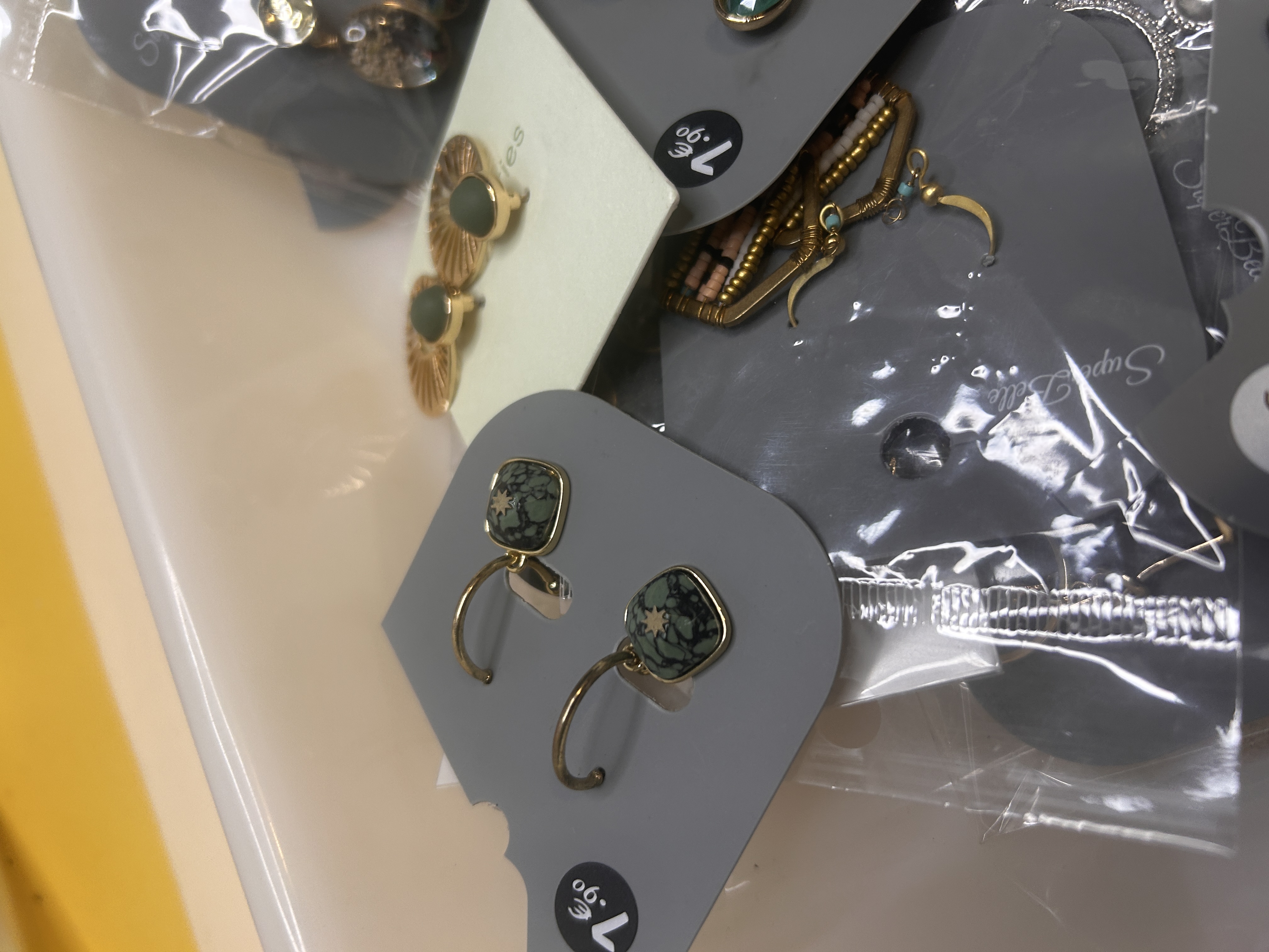 Vista detallada de pendientes de bisutería, incluyendo pendientes de aro cuadrados con piedras verdes jaspeadas y pendientes de botón dorados en forma de mariposa.