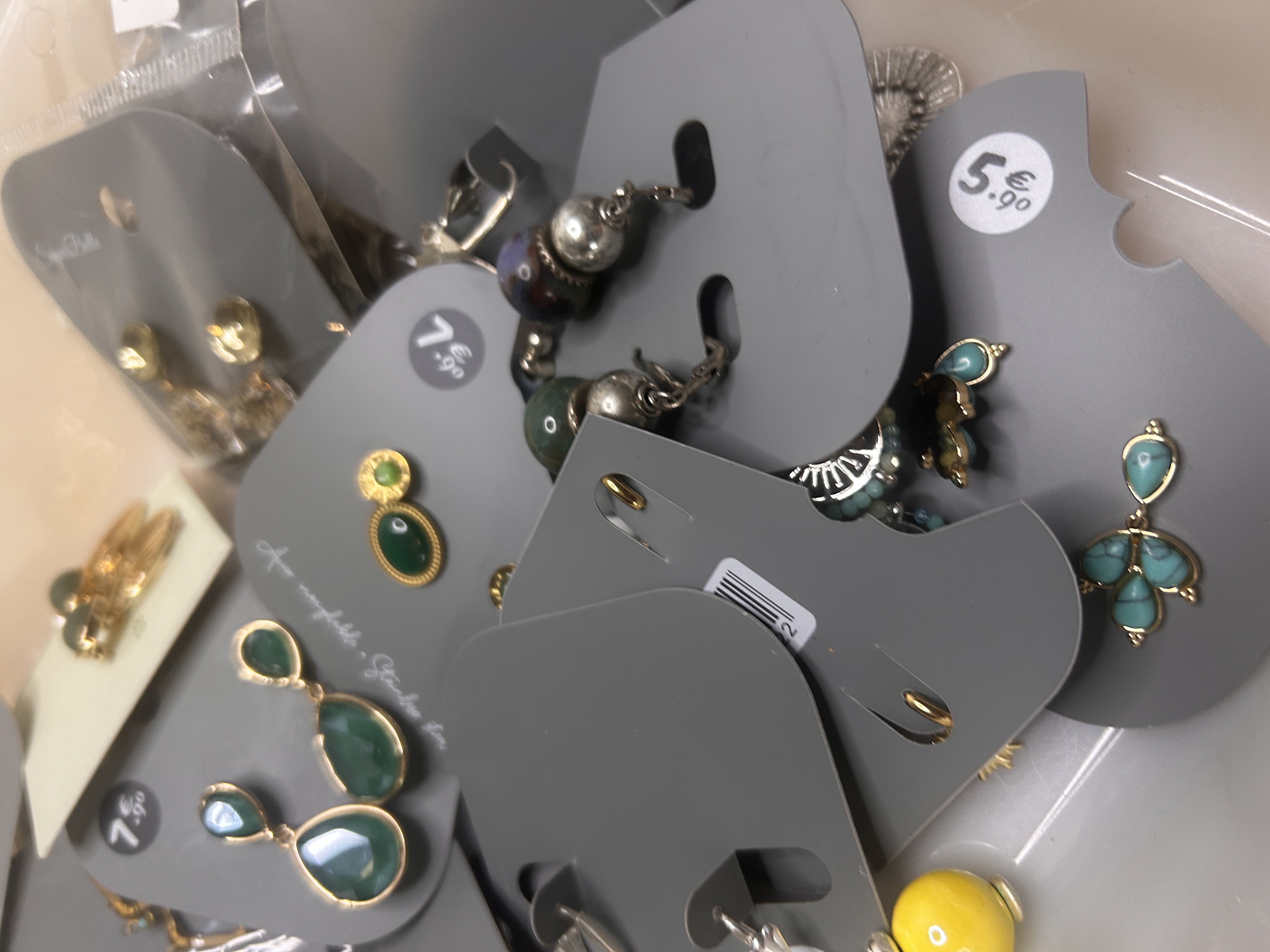Surtido de pendientes de bisutería con enfoque en pendientes colgantes de mariposa turquesa, pendientes colgantes esféricos amarillos y varios estilos de pendientes de botón y colgantes.
