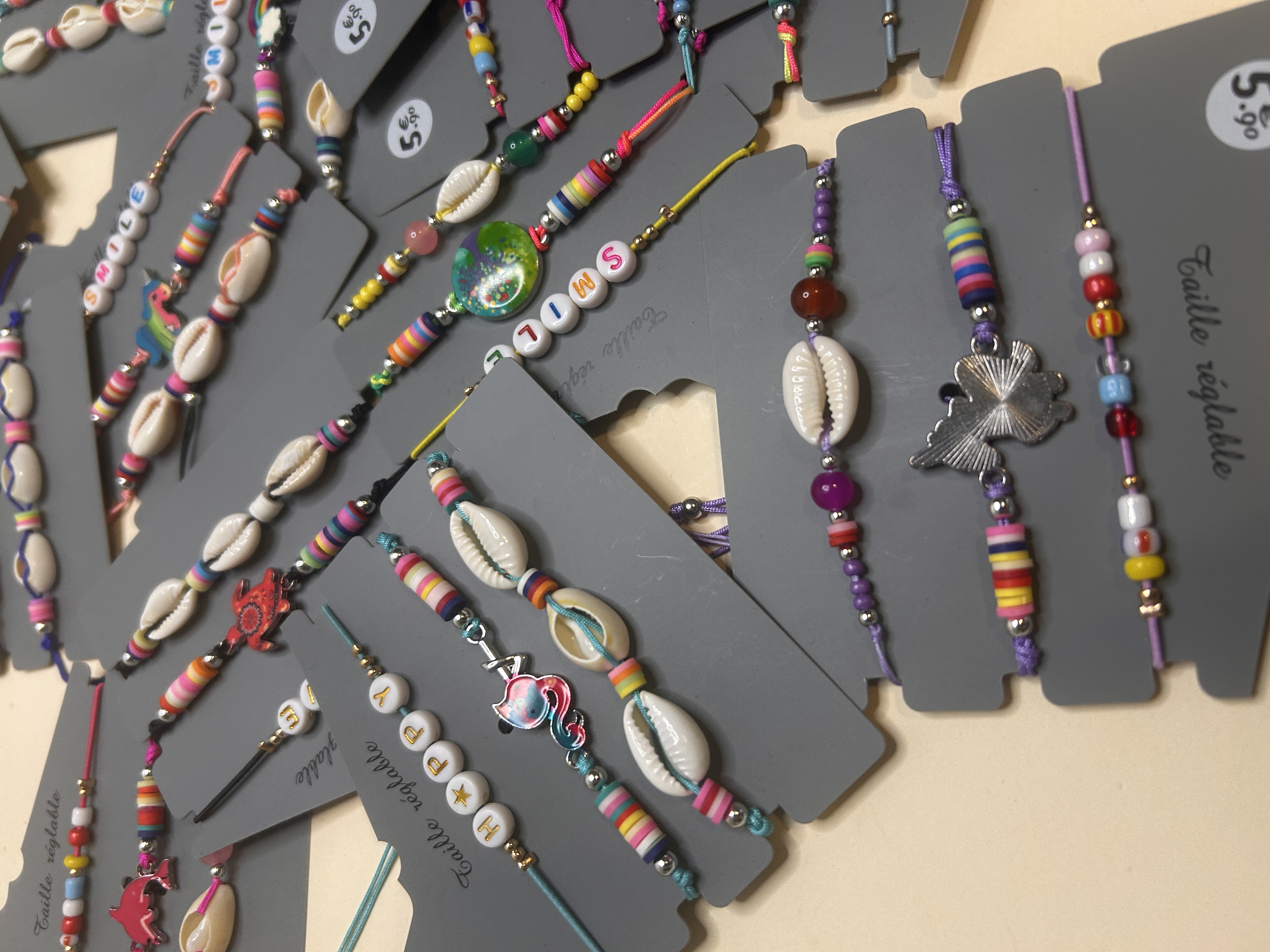 Detalle de cerca de varias pulseras de bisutería coloridas, mostrando conchas de cauri, cuentas de colores brillantes y abalorios divertidos como una tortuga roja y cuentas de letras que forman 'HAPPY'.