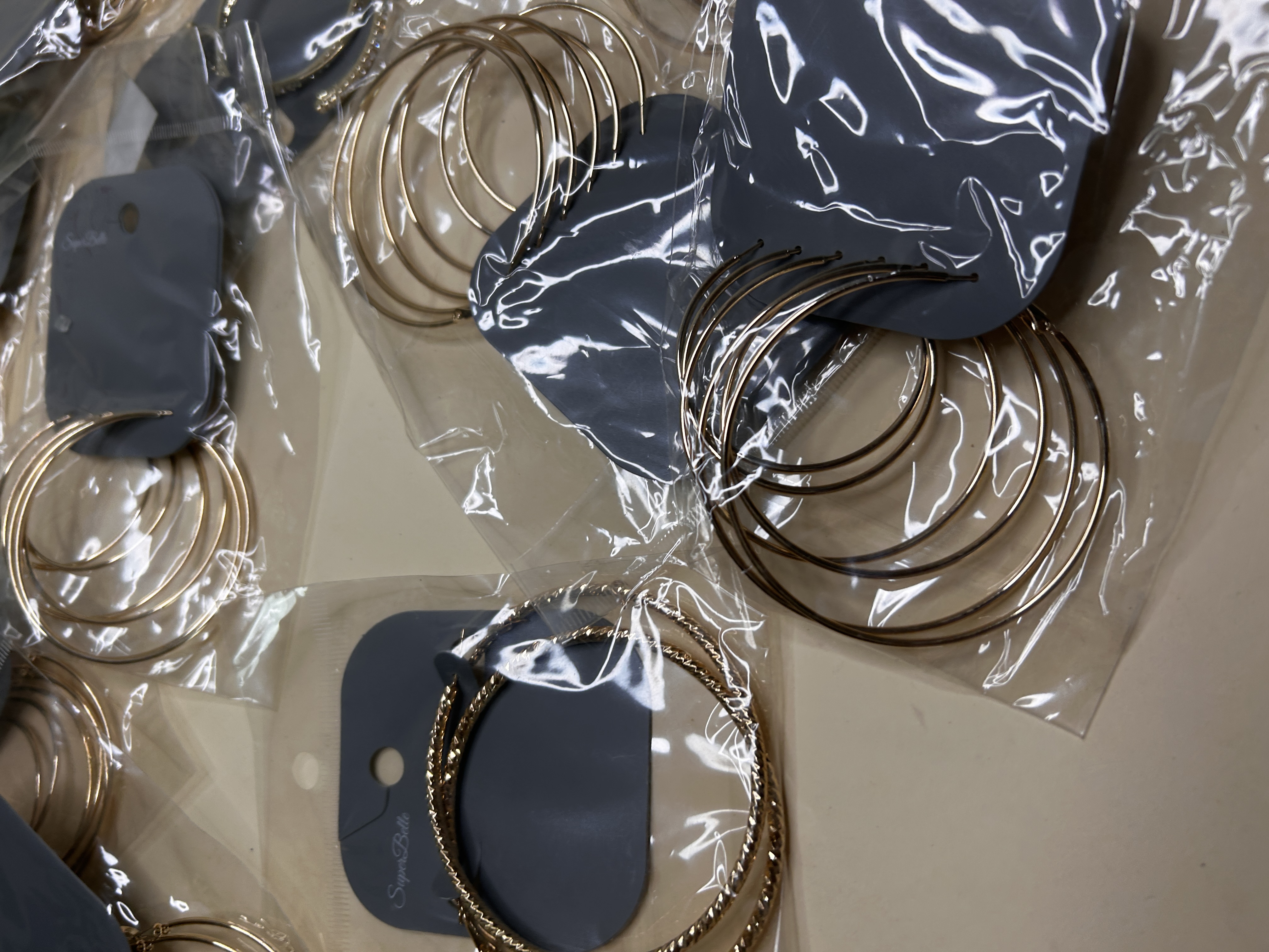 Detalle de aros dorados lisos y trenzados en fundas transparentes — lote de pendientes originales, detalle del acabado · Lotes Bisutería (HOOP-203)