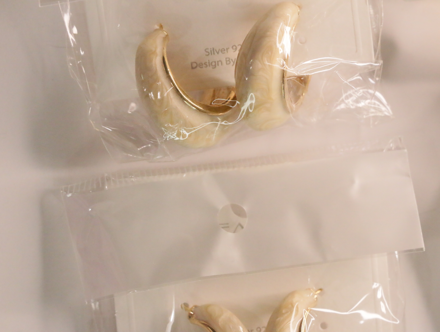 Pendientes de aro crema jaspeado en envoltorio transparente — lote de bisutería originales, detalle del acabado · Lotes Bisutería (LT045)